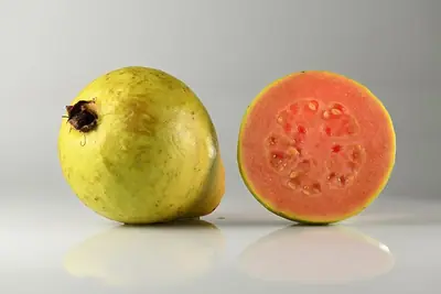 A guava beside one cut in half, pink inside